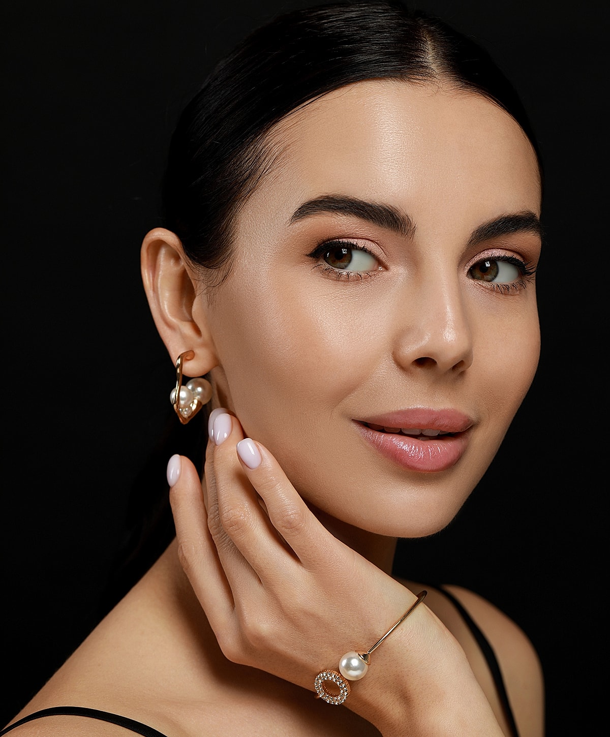 Woman showcasing elegant pearl jewelry on black background.