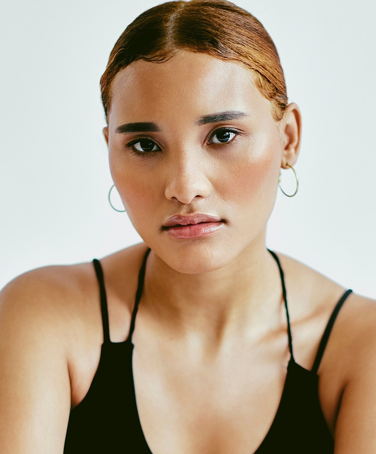 Woman with makeup and styled hair, neutral backdrop.