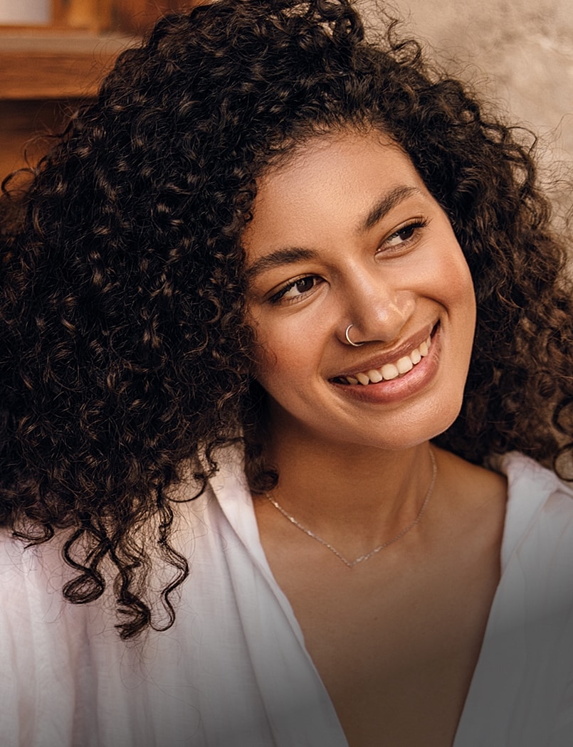 Woman smiling with curly hair and necklace.