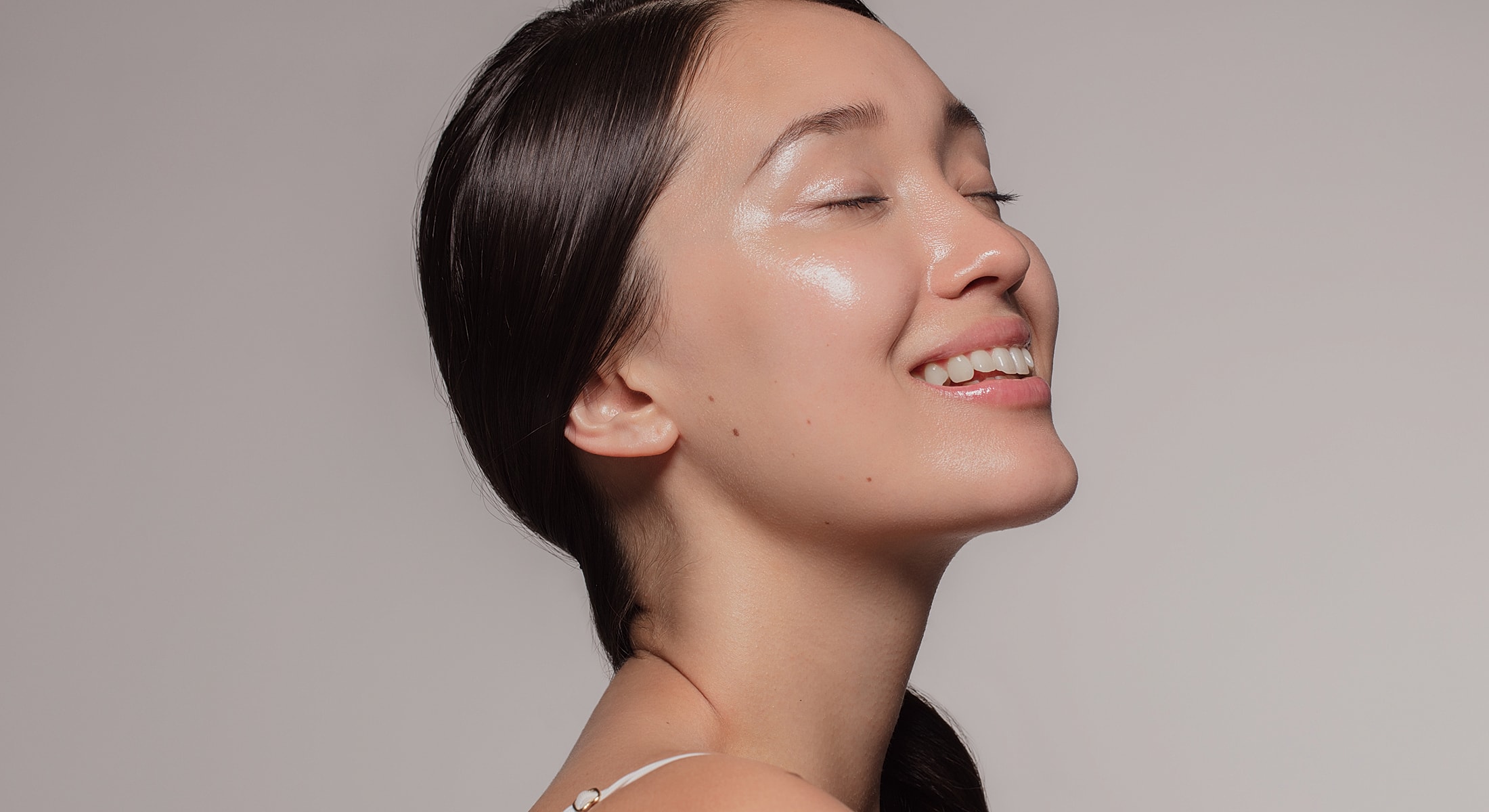 Smiling woman with closed eyes and shiny skin.